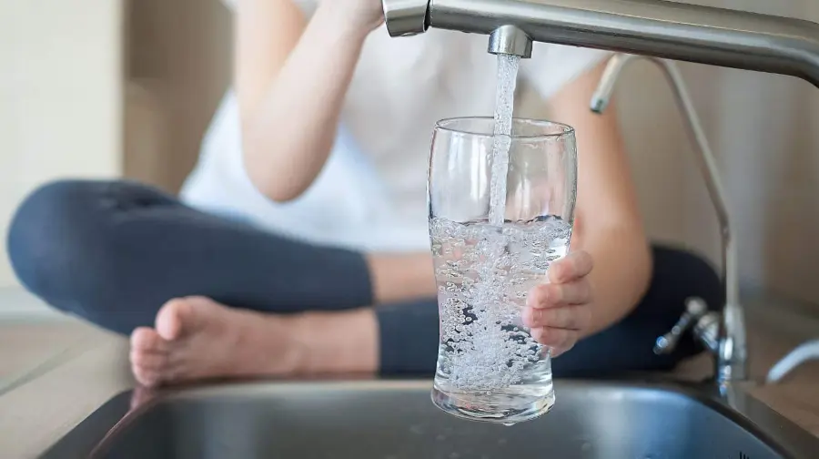 Happy customer filling a clear glass with fresh, sparkling, pure drinking water straight from the kitchen faucet — made possible by United Water Softeners’ Sentinel water softener and filtration systems in Houston.