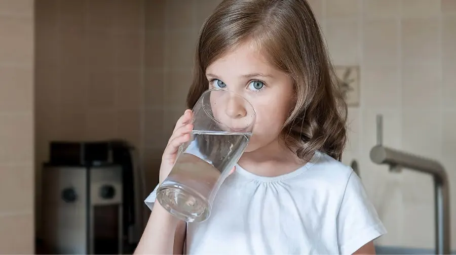 Adorable young girl with beautiful blue eyes happily drinking pure, crystal-clear Reverse Osmosis (RO) filtered water from a glass – made possible by United Water Softeners’ PureGuard system in Houston.
