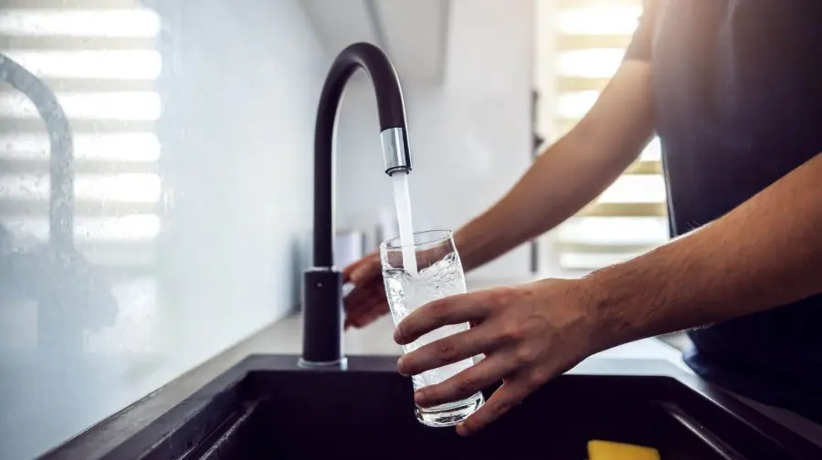 Customer filling a clear glass with crisp, pure Reverse Osmosis (RO) drinking water from the kitchen faucet — delivered by United Water Softeners’ PureGuard RO system in Houston.