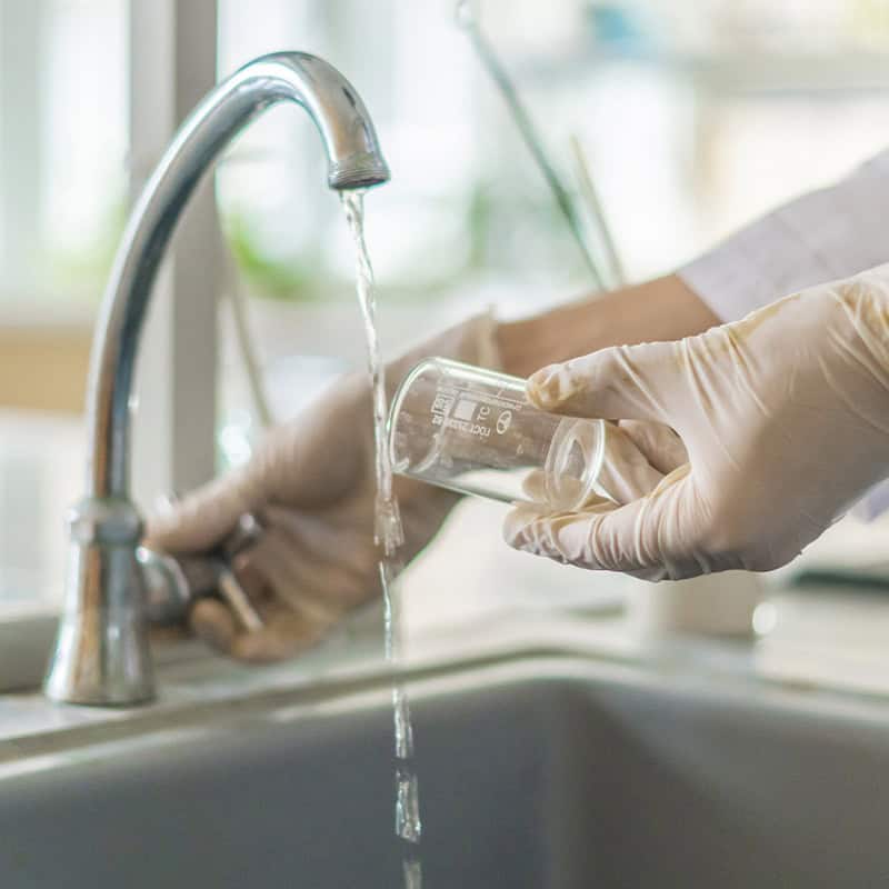 Gloved hands collecting a water sample from a kitchen faucet for water quality testing Gloved hands collecting a water sample from a kitchen faucet for water quality testing