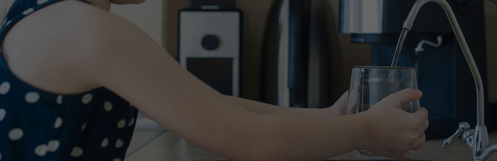 Young child happily filling a clear glass with fresh, pure water straight from the kitchen faucet – safe, delicious drinking water made possible by United Water Softeners, Houston’s best water company