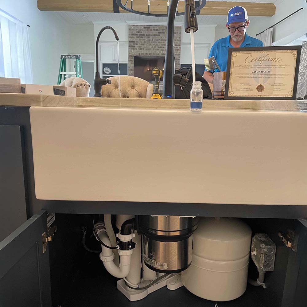 Professional reverse osmosis (RO) drinking water system installation by United Water Softeners in Fulshear, TX. Custom matte black faucet on a white farmhouse sink dispenses the cleanest and purest water in Houston, shown in a clear sample bottle, certified