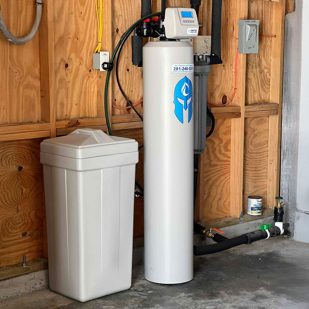 Neatly installed Sentinel Guardian Package water softener by United Water Softeners. Professional gray softener tank with iconic blue Spartan helmet logo, white brine tank, and clean piping mounted against a wooden garage wall – premium water treatment at an affordable price.