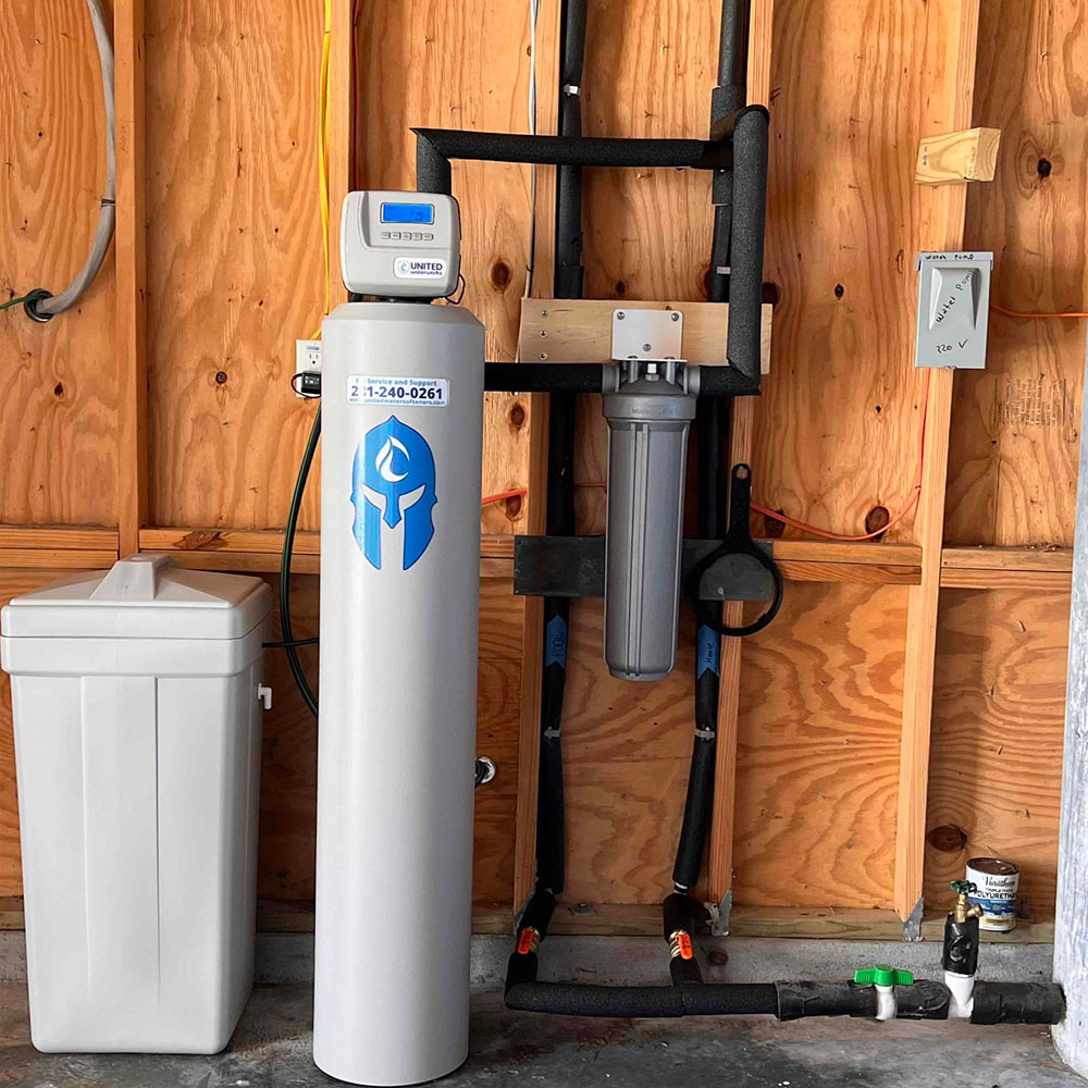 Neatly installed Sentinel Guardian Package water softener by United Water Softeners. Professional gray softener tank with iconic blue Spartan helmet logo, white brine tank, and clean piping mounted against a wooden garage wall – premium water treatment at an affordable price.
