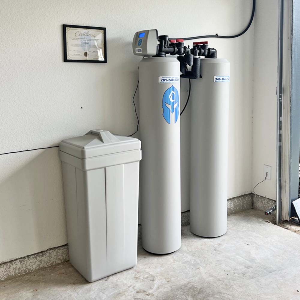 Elite Package whole-house water softener and carbon filtration system professionally installed inside the garage in Conroe, Texas by United Water Softeners – Houston’s #1 rated water company. Certificate of installation visible.