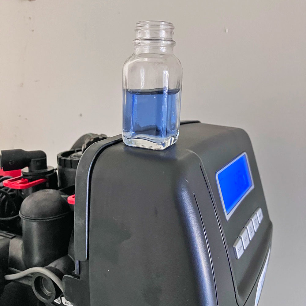 Pure clean water sample in a glass bottle on top of a United Water Softeners control valve, showcasing high-quality water treatment system.